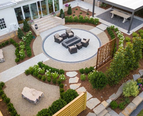 A classic landscape design with modern twists, including a fire pit, beautiful plants and shrubs, a covered dining table, and custom rock benches engraved with the family's favorite quotes. This outdoor living space was designed and built by R&R Landscaping.