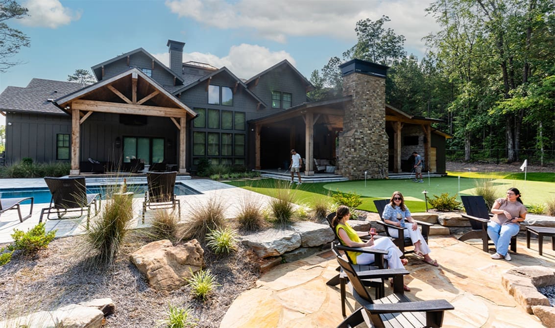 A spectacular backyard with a swimming pool, fire pit, sitting area, and putting green with friends hanging out and chatting. This project was designed and built by R&R Landscaping.