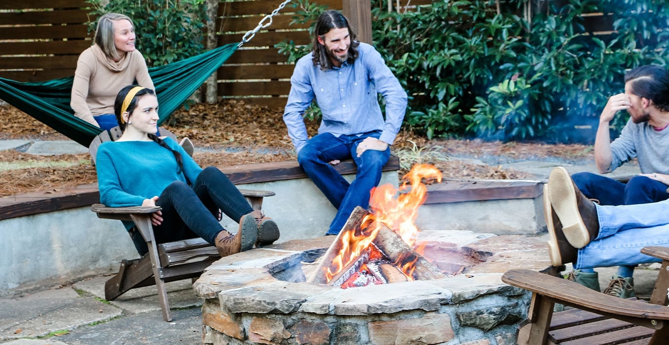A cozy fire pit with friends sitting around and chatting. This project was designed and built by R&R Landscaping.