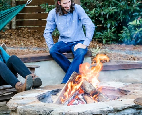A cozy fire pit with friends sitting around and chatting. This project was designed and built by R&R Landscaping.